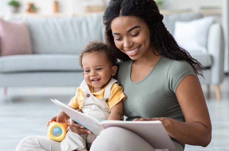 A smiling woman reads to a laughing toddler